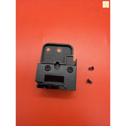 Black plastic electronic component or mounting bracket with two red dots and visible screw holes.