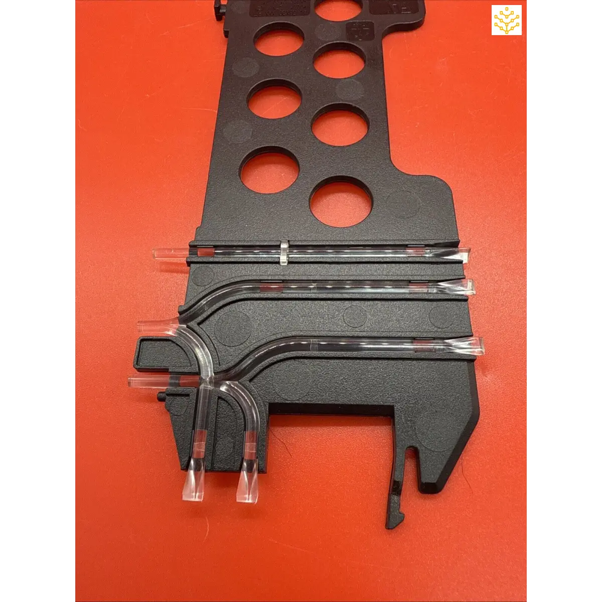 Black plastic slot car track piece with multiple holes and curved sections.