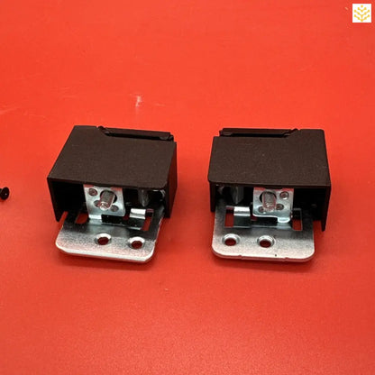 Two black electrical relays or switches with metal mounting brackets on a red surface.