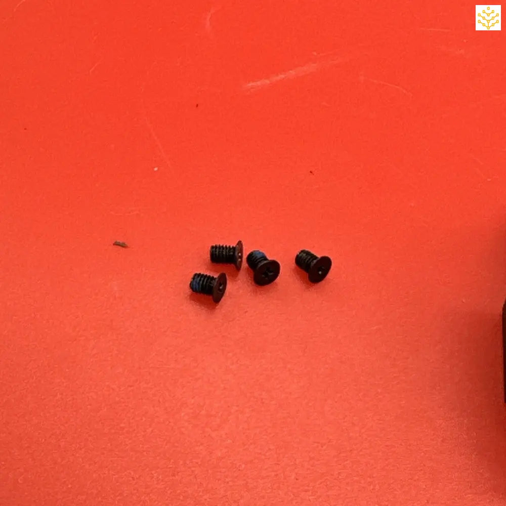 Four small black screws on a bright red surface.