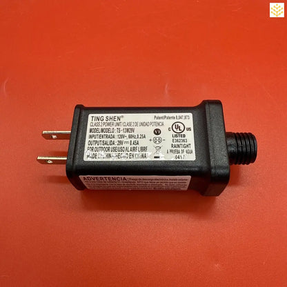 Black power adapter with electrical prongs and UL certification markings.