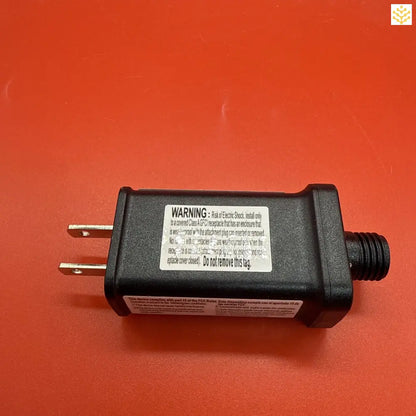 Black electrical power adapter with warning label and prongs.