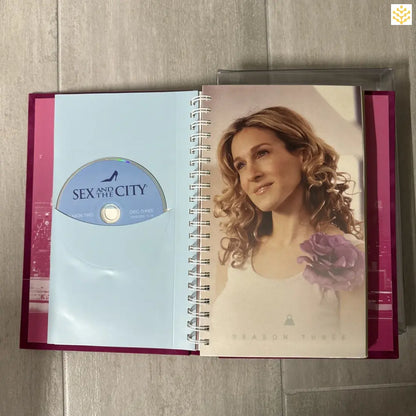 Pink-bound notebook or journal containing a Sex and the City DVD disc and promotional photo.