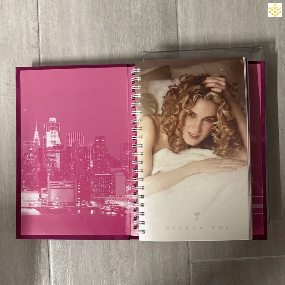 Pink spiral-bound book or journal featuring a cityscape silhouette and a sepia-toned portrait photograph.