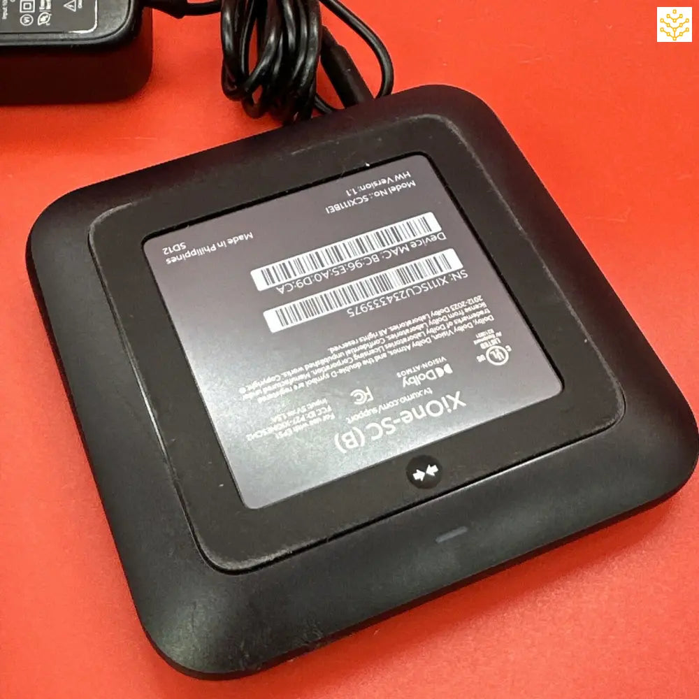 Electronic device with a square shape and a display screen, likely a router or modem.