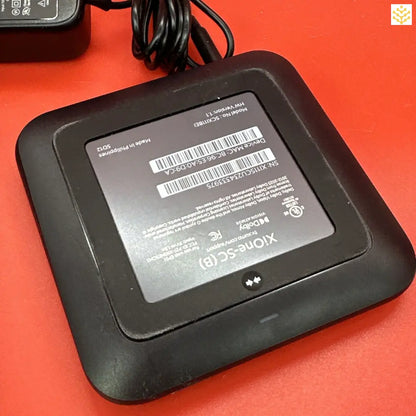 Electronic device with a square shape and a display screen, likely a router or modem.